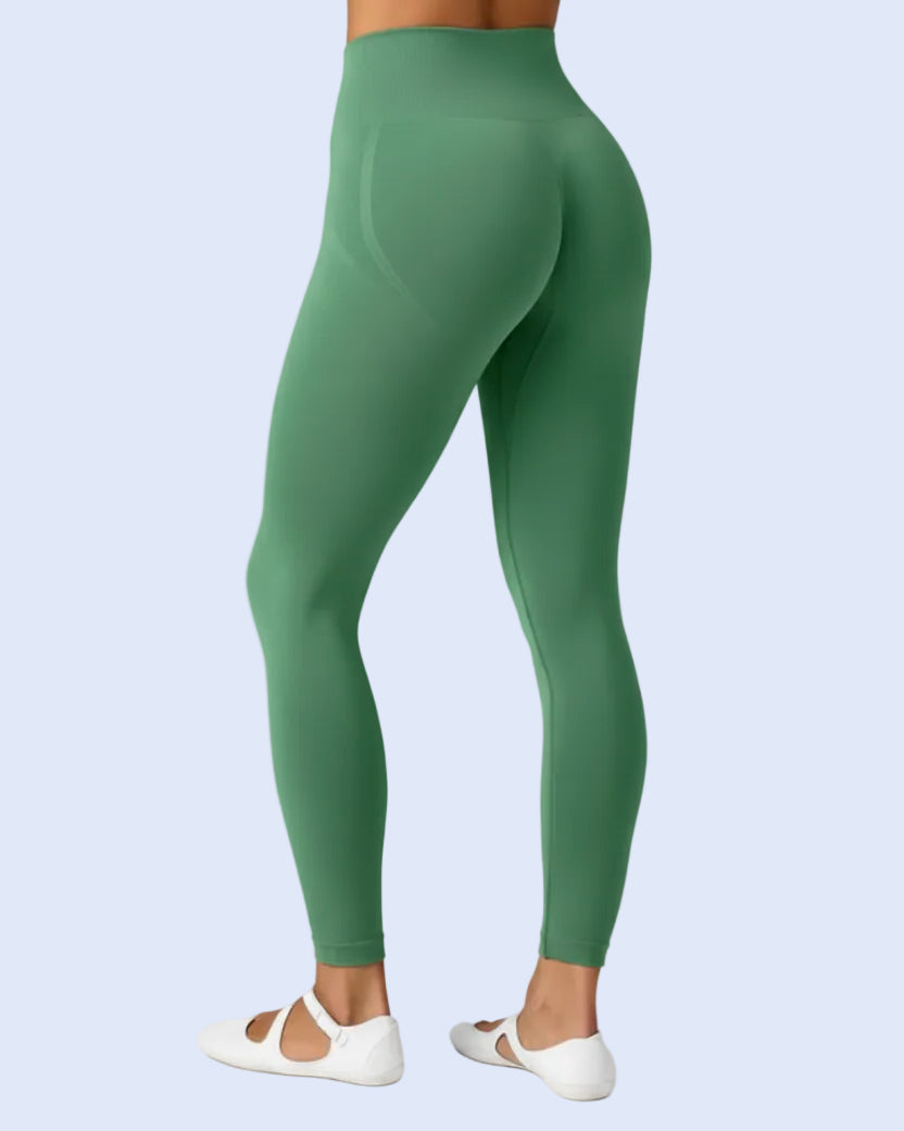 A model shown from the back wearing high-waisted green leggings and bright pink ballet flats against a light gray studio background.