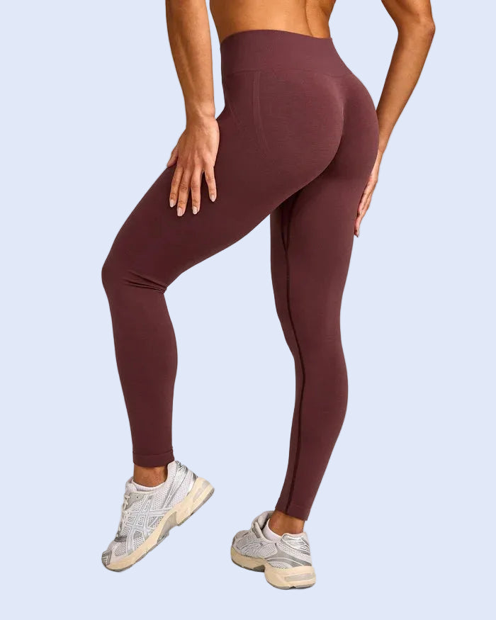 A model wearing high-waisted, form-fitting leggings in a deep burgundy color, shown from a rear three-quarter angle against a light gray studio background.