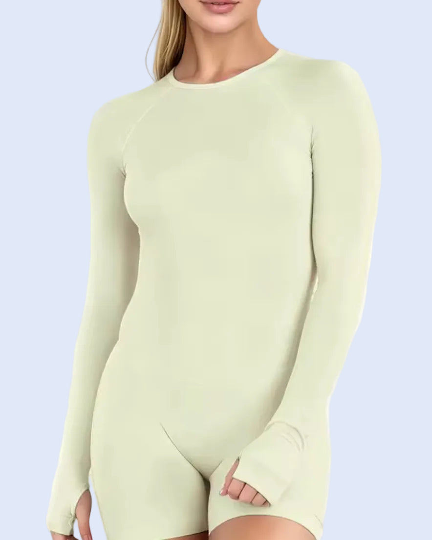 A woman wearing a pale sage green long-sleeve bodysuit with thumbholes, shown from the neck down against a plain white background.