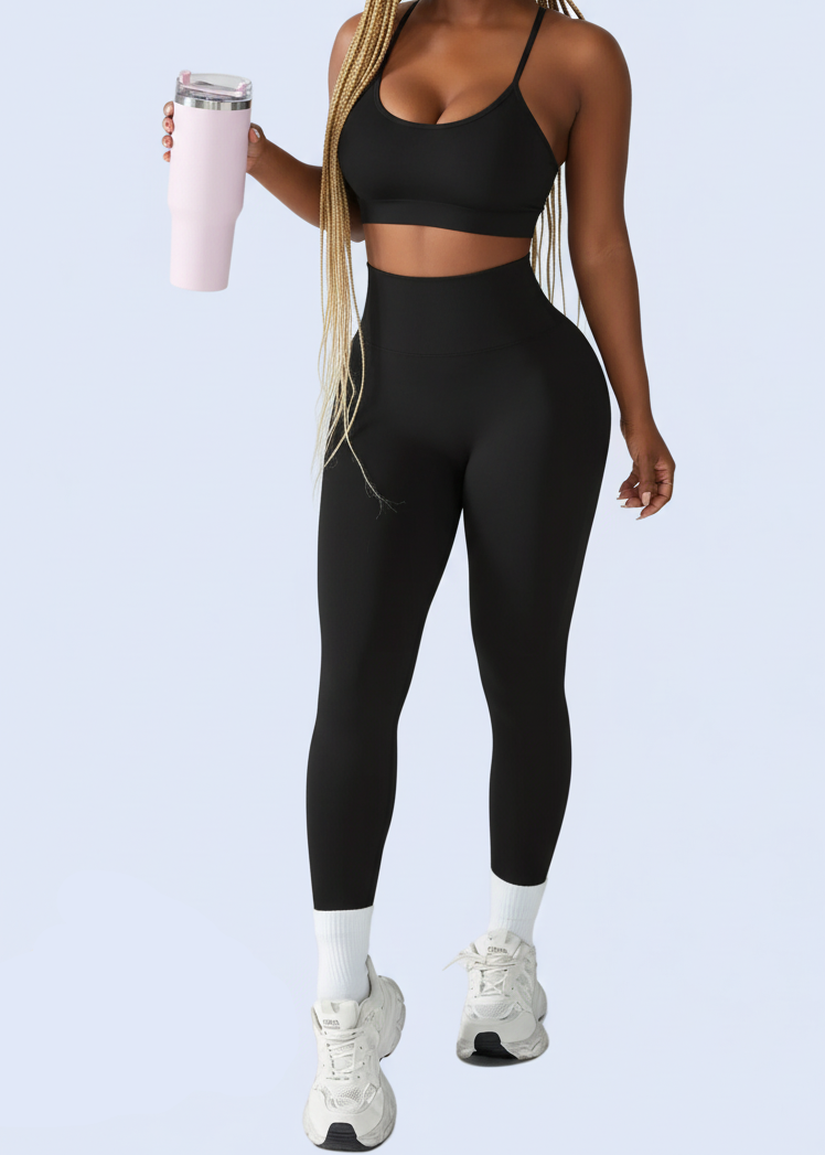 Woman in black athletic wear holding a pink water bottle on a white background