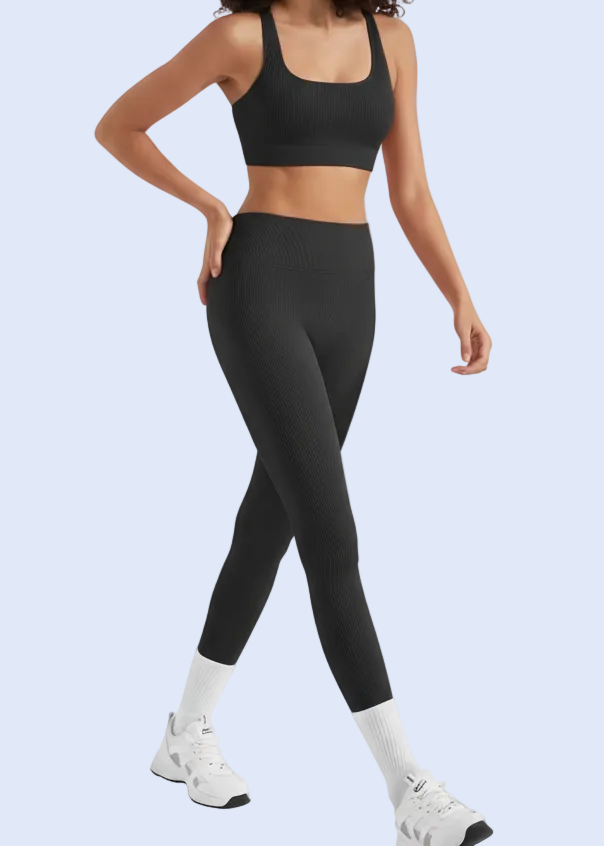 Person wearing black athletic outfit with white sneakers on a plain background