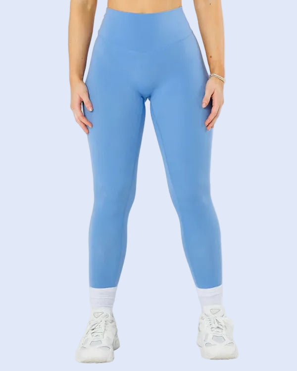 A model wearing high-waisted, light blue athletic leggings, a matching blue sports bra, white socks, and white sneakers, shown from the waist down against a light gray studio background.
