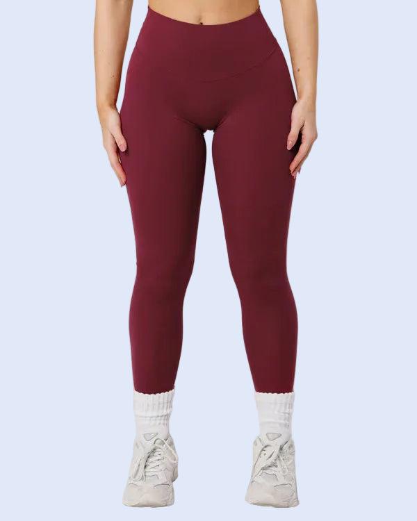 Person wearing maroon leggings and a sports bra on a light gray background