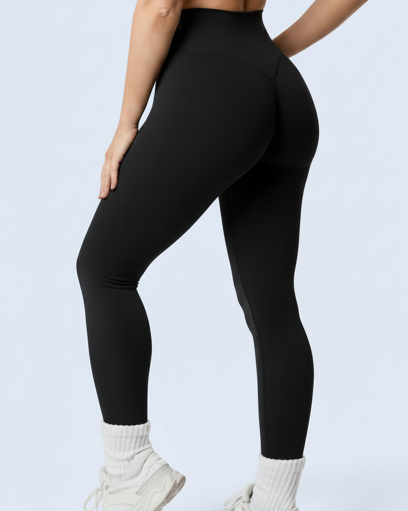 Woman wearing black athletic leggings and sports bra on a light gray background