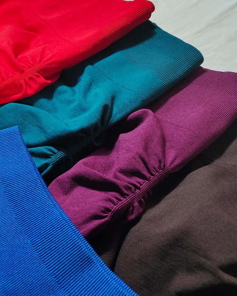 Stack of colorful folded fabrics in red, green, purple, and brown.