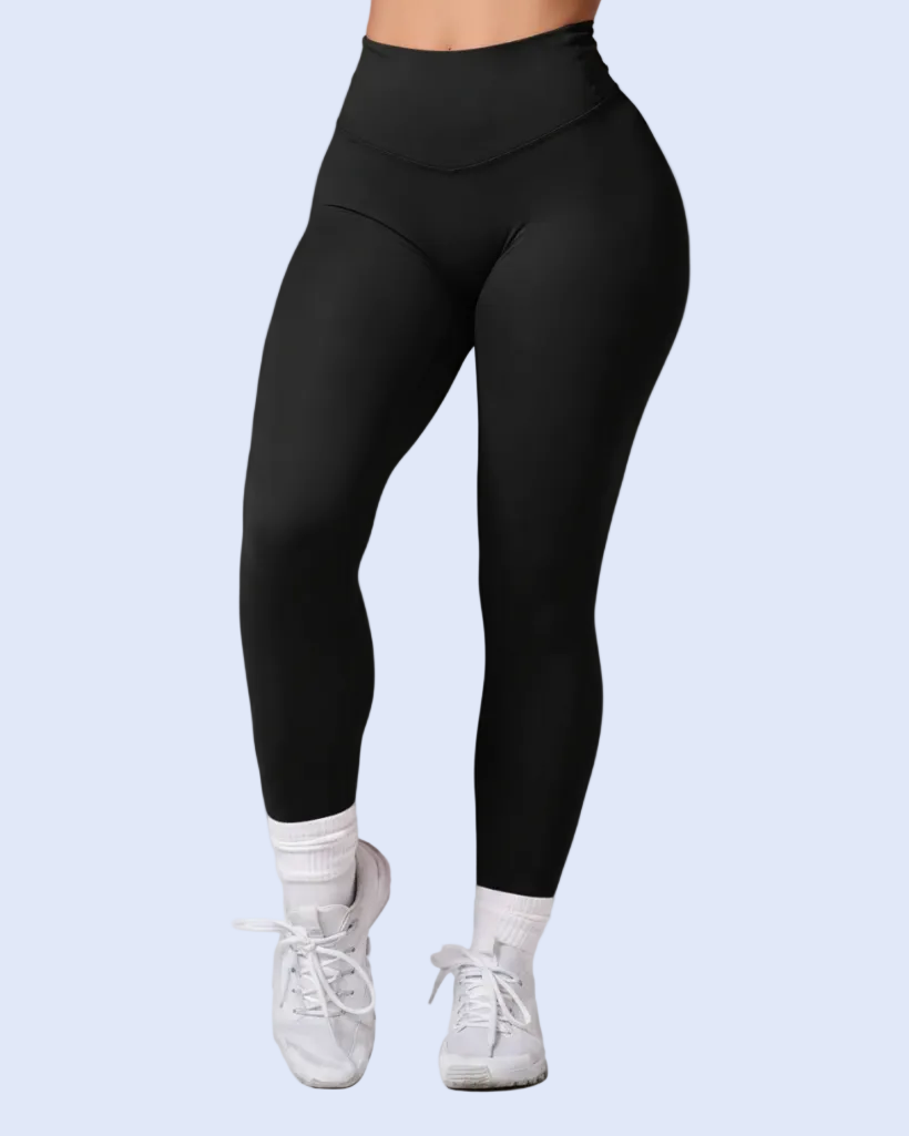 Black high-waisted leggings worn by a model, paired with white socks and white sneakers, shown from the waist down against a light blue background.