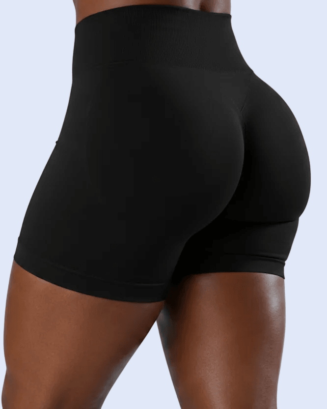 Rear view of a model wearing black high-waisted athletic shorts against a light gray studio background.