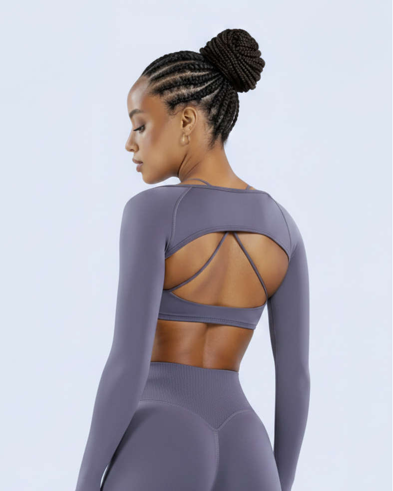 A woman modeling a matching long-sleeve athletic set in a dusty purple color, shown from the back against a light blue studio background.