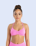 A woman wearing a bright pink sports bra and matching high-waisted athletic bottoms, photographed against a light gray studio background.