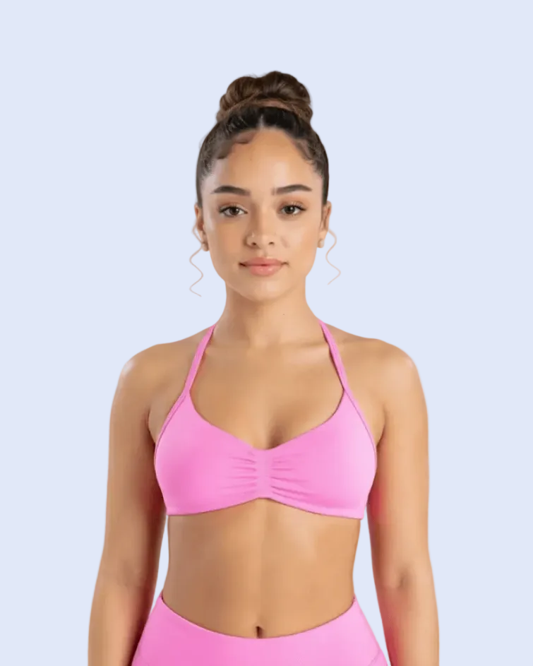 A woman wearing a bright pink sports bra and matching high-waisted athletic bottoms, photographed against a light gray studio background.