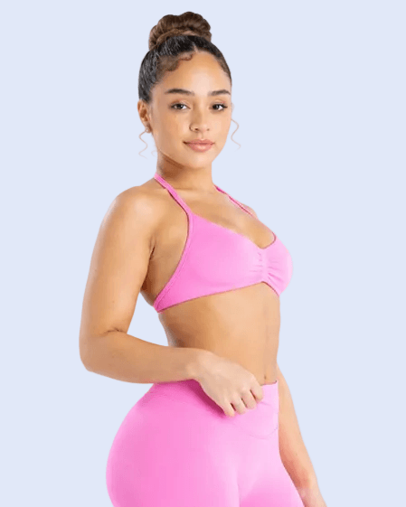 A woman modeling a bright pink two-piece activewear set consisting of a ruched sports bra and high-waisted leggings, set against a light gray studio background.