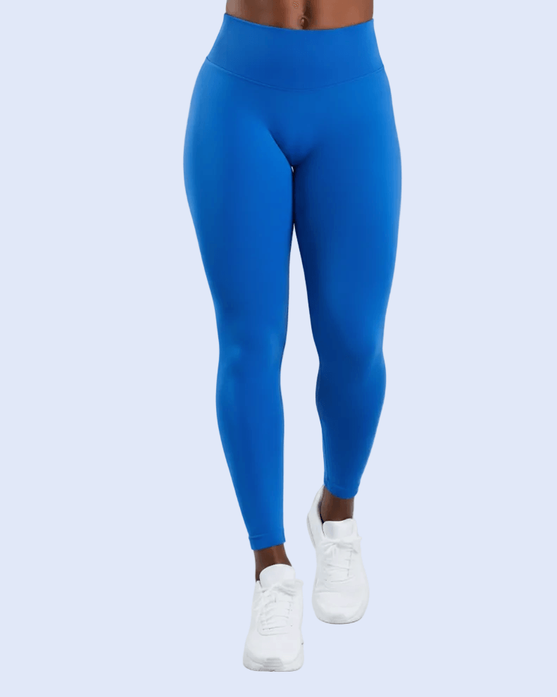A model from the waist down wearing bright royal blue high-waisted leggings and white sneakers, standing against a light gray studio background.