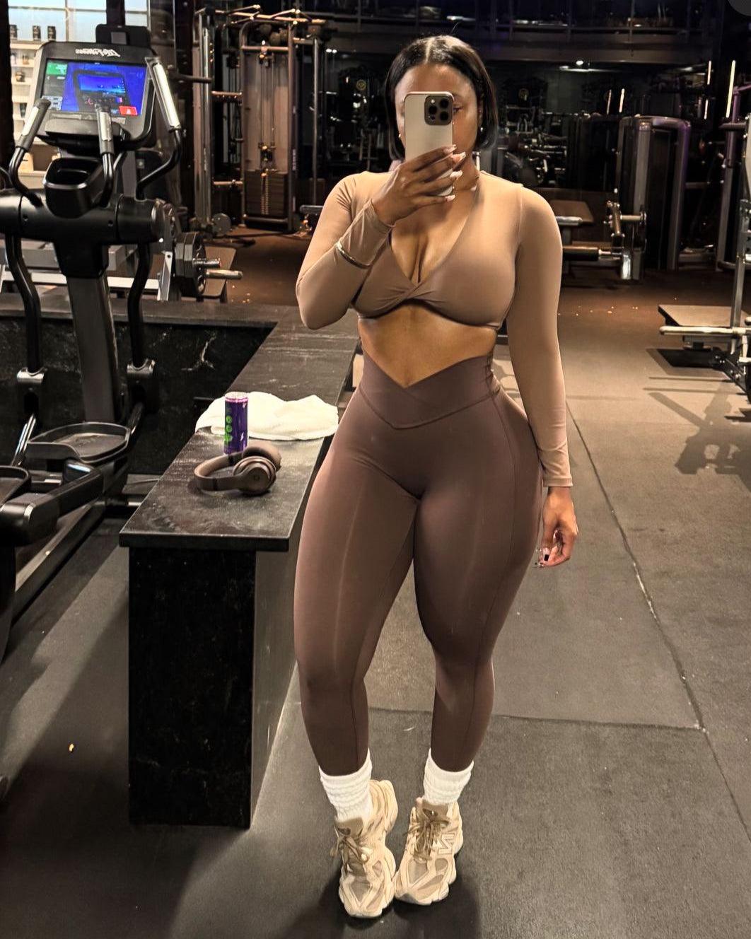 Person taking a mirror selfie in a gym wearing a beige sports bra and leggings.