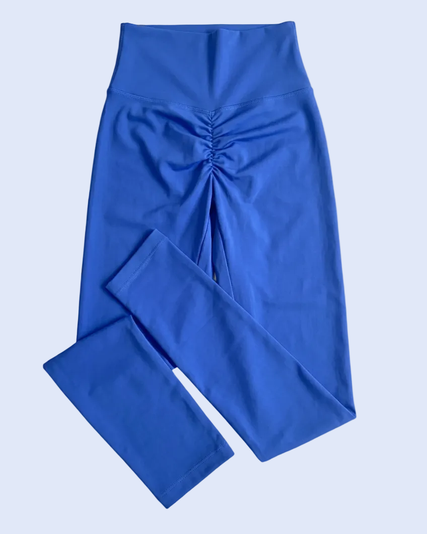 A pair of royal blue high-waisted leggings with a ruched front detail, laid flat on a light blue background.