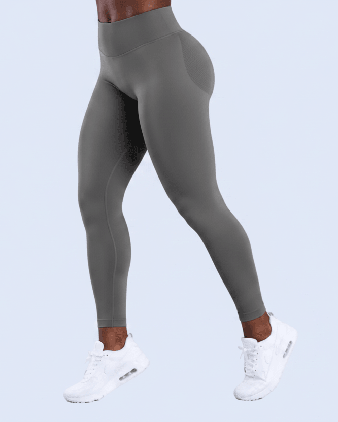 A model wearing high-waisted, form-fitting gray leggings and white sneakers, shown from the waist down against a solid light blue background.
