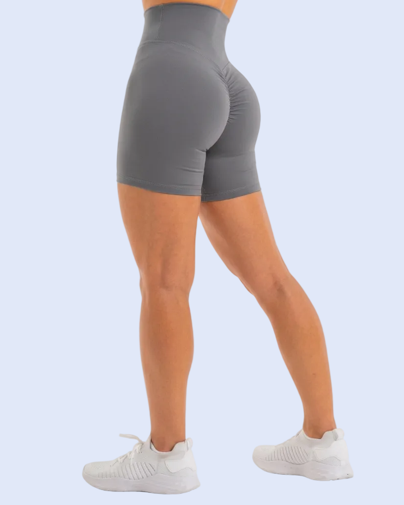 A person shown from the waist down wearing high-waisted gray athletic shorts and white sneakers, photographed against a plain light blue studio background.