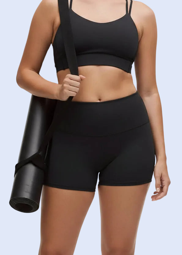 Woman in black athletic wear holding a yoga mat on a white background