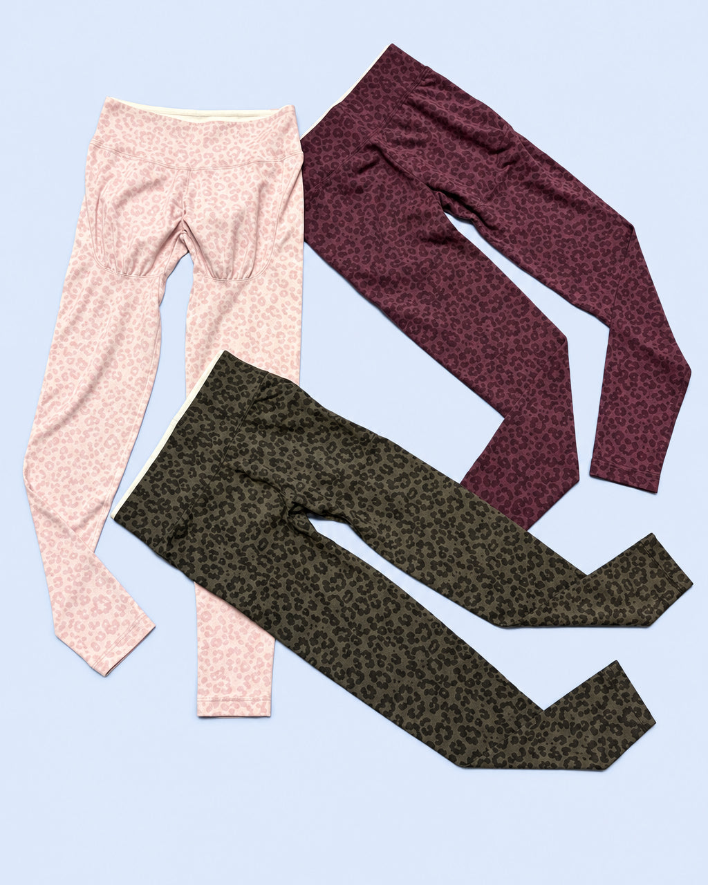Three pairs of women's leggings laid flat on a gray background: one light pink solid, one dark burgundy leopard print, and one dark brown leopard print.