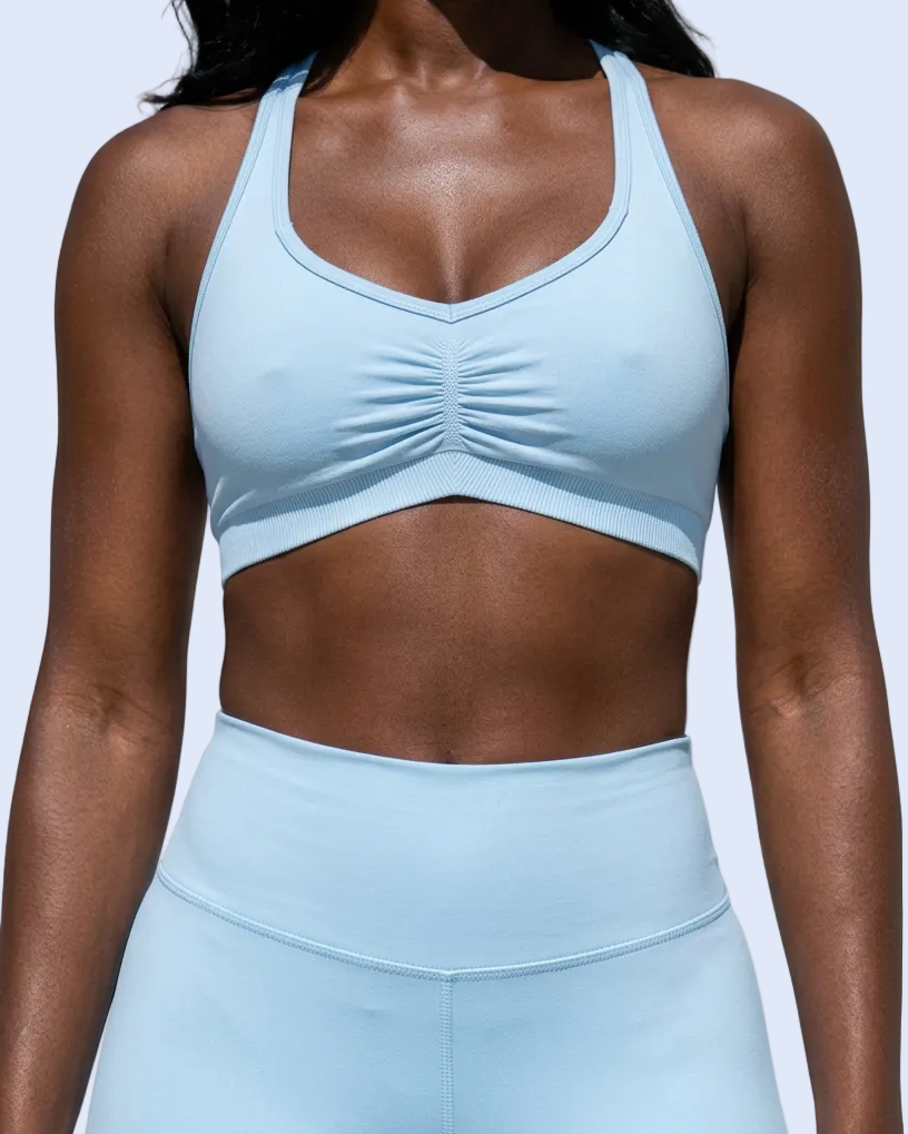 A woman wearing a light blue athletic sports bra and matching high-waisted leggings against a light gray studio background.