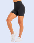 Black high-waisted biker shorts worn by a model, paired with white sneakers, shown from the waist down on a white studio background.