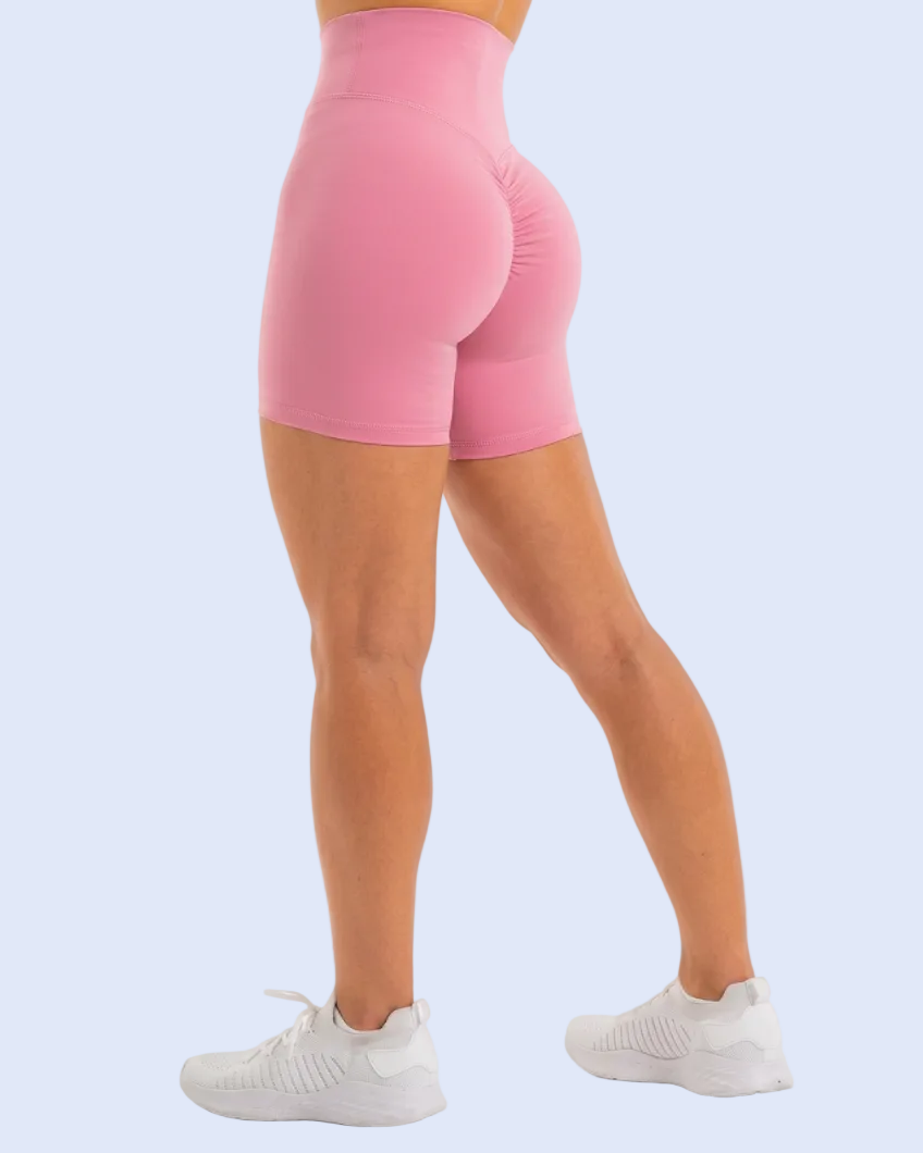 A person wearing bright pink high-waisted biker shorts, shown from the waist down in a side profile against a light blue studio background.