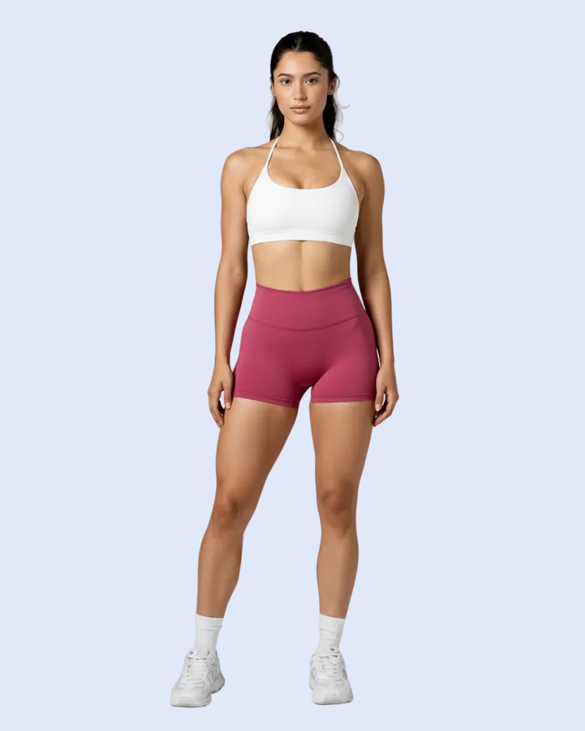 A woman modeling a white sports bra and high-waisted magenta athletic shorts against a light gray studio background.