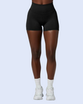 A model from the waist down wearing black high-waisted athletic shorts, white crew socks, and white sneakers, set against a solid light blue background.