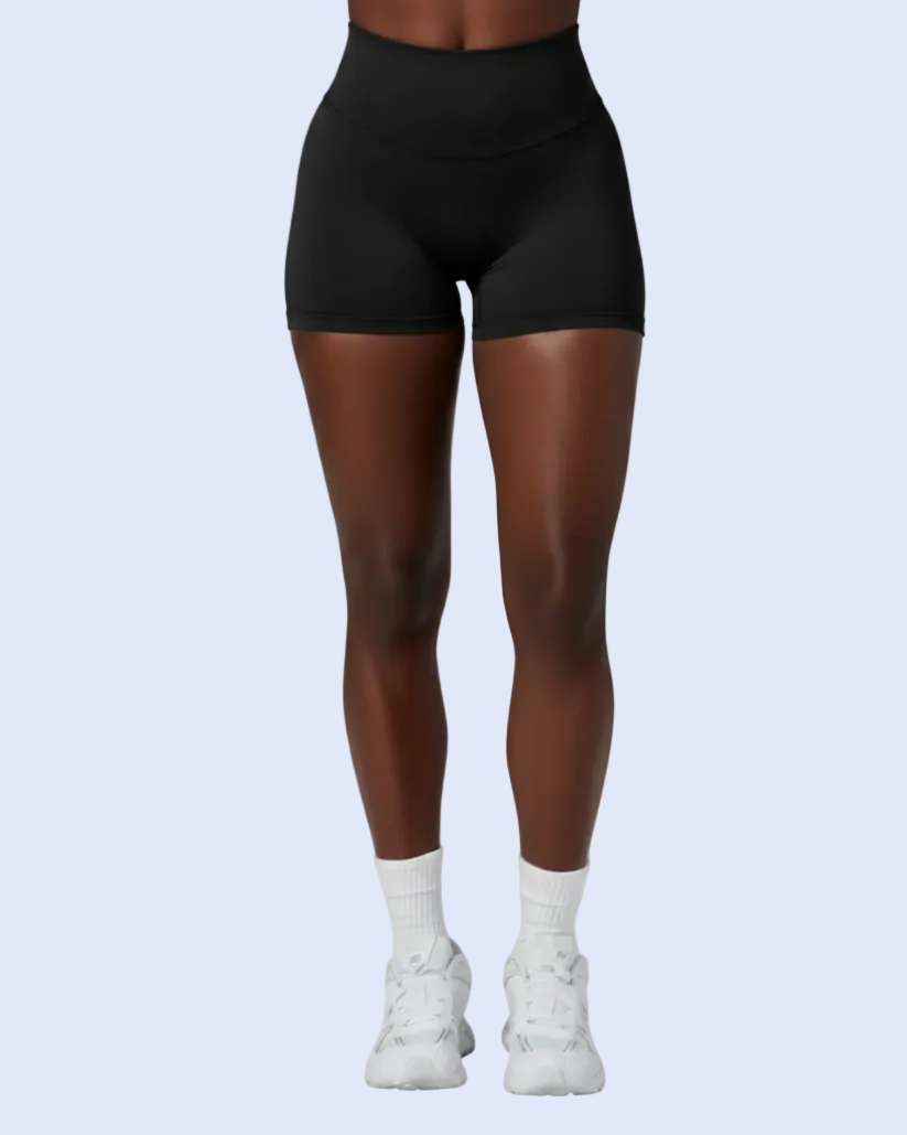 A model from the waist down wearing black high-waisted athletic shorts, white crew socks, and white sneakers, set against a solid light blue background.