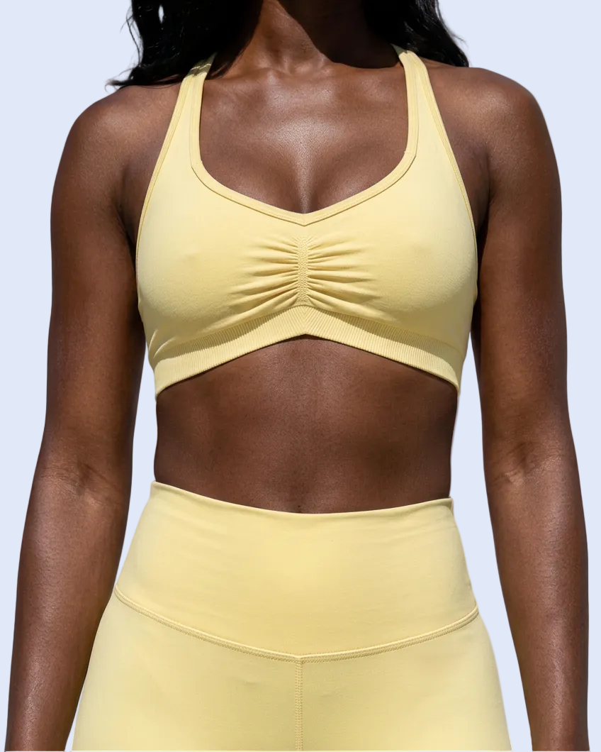A woman wearing a pale yellow sports bra and matching high-waisted leggings against a light blue-gray studio background.