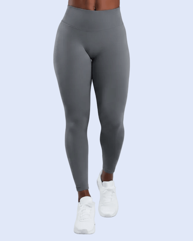 A person from the waist down wearing high-waisted gray leggings and white sneakers, shown against a light blue studio background.